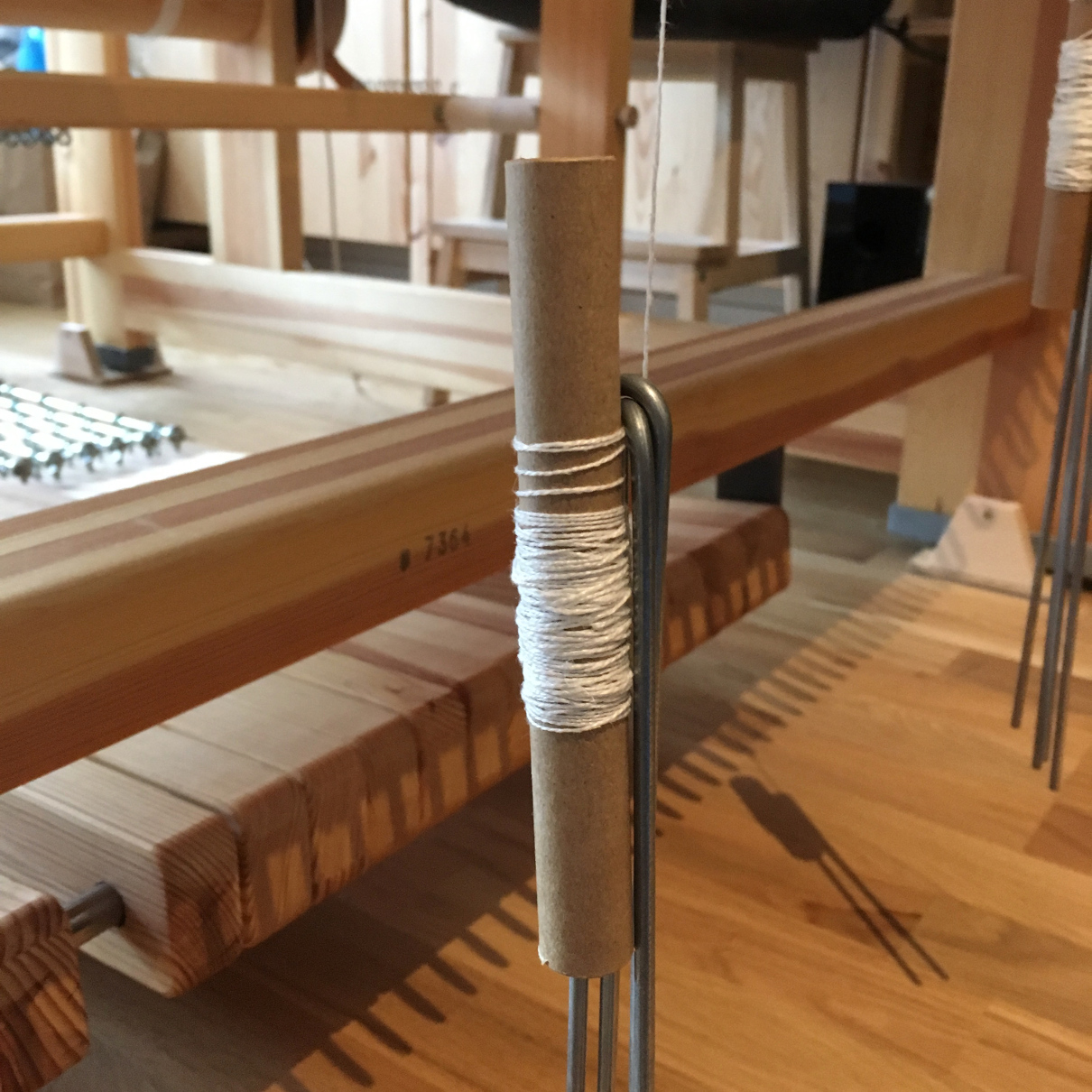 Photograph of a bobbin dangling at the back of the loom, weighted down by several U-shaped damask weights.