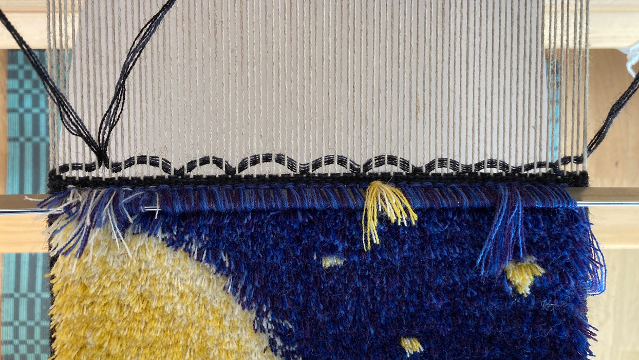 A pile carpet in progress on the loom, showing the weft forming many small arcs.